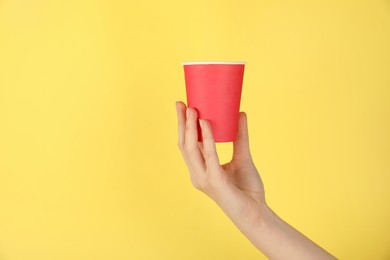 Photo of Woman holding paper cup on yellow background, closeup. Mockup for design