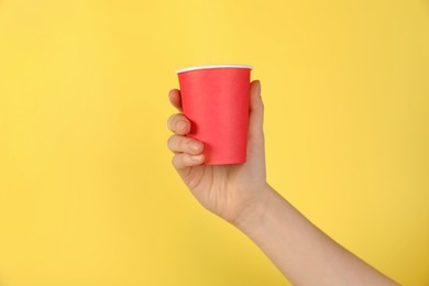 Photo of Woman holding paper cup on yellow background, closeup. Mockup for design
