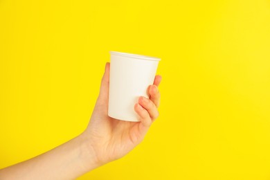 Photo of Woman holding paper cup on yellow background, closeup. Mockup for design