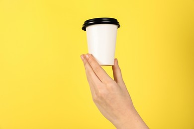 Photo of Woman holding paper cup on yellow background, closeup. Mockup for design