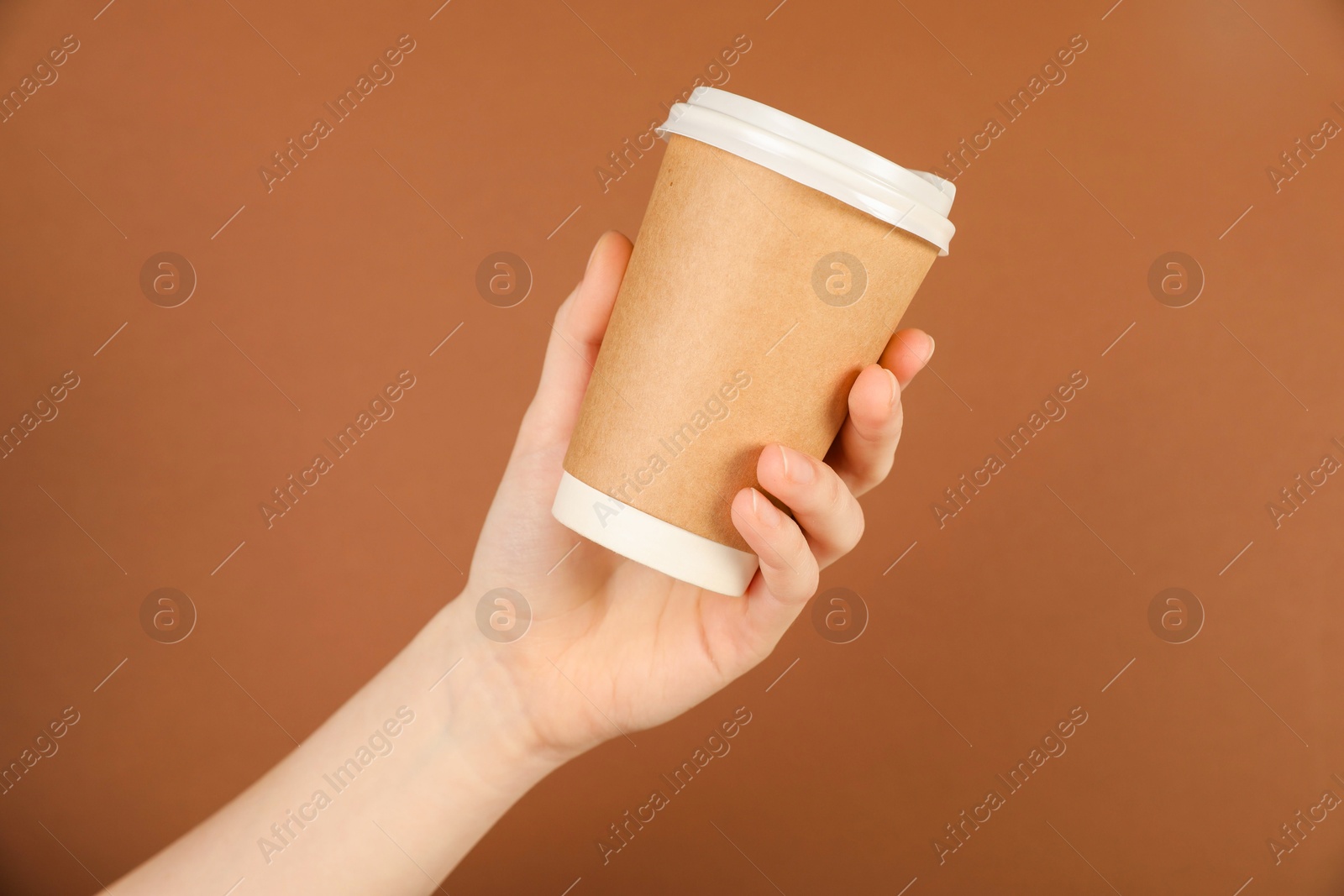 Woman holding paper cup on brown background, closeup. Mockup for design Photo of Woman holding paper cup on brown background, closeup. Mockup for design