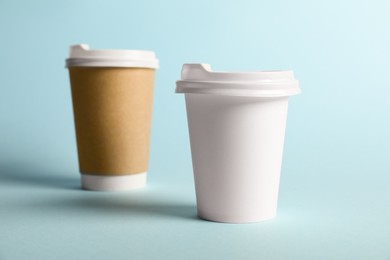 Photo of Paper cups on light blue background, selective focus. Mockup for design