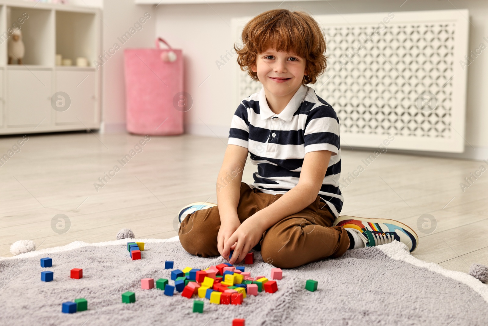 Photo of Little boy playing with colorful cubes on floor at home