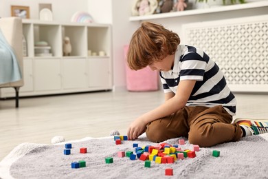 Photo of Little boy playing with colorful cubes on floor at home, space for text