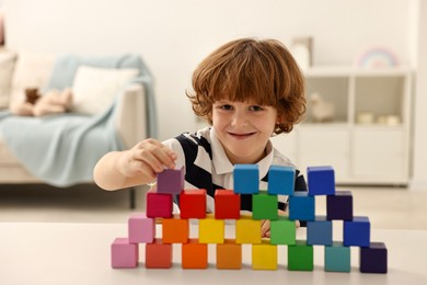 Photo of Little boy stacking colorful cubes at white table indoors