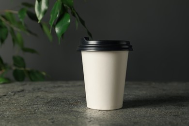 Photo of Paper cup on grey textured table indoors, closeup. Mockup for design