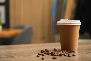 Photo of Paper cup and coffee beans on wooden table indoors. Mockup for design