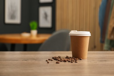 Photo of Paper cup and coffee beans on wooden table indoors. Mockup for design