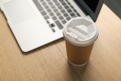 Photo of Paper cup and laptop on wooden table, closeup. Mockup for design
