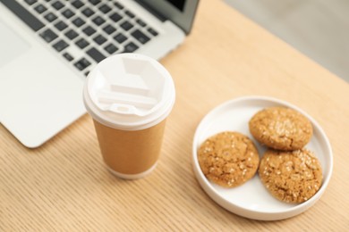 Photo of Paper cup, plate with cookies and laptop on wooden table, closeup. Mockup for design