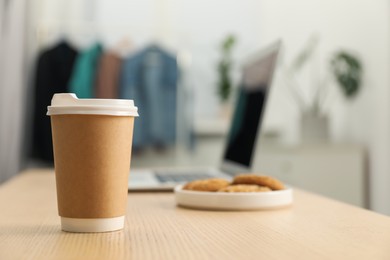 Photo of Paper cup, plate with cookies and laptop on wooden table indoors, closeup. Mockup for design