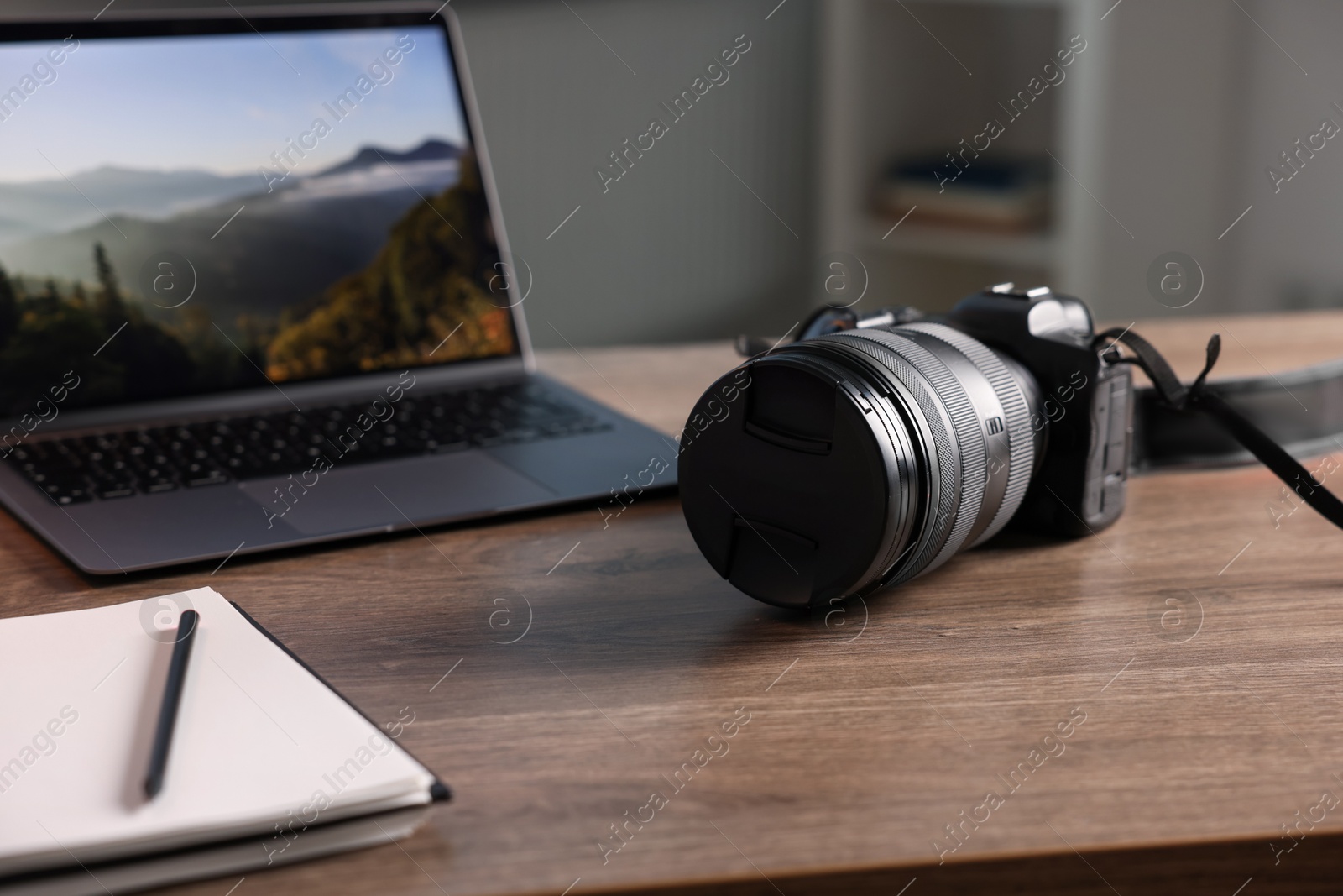 Photo of Professional photo camera, laptop and notepad on wooden desk indoors