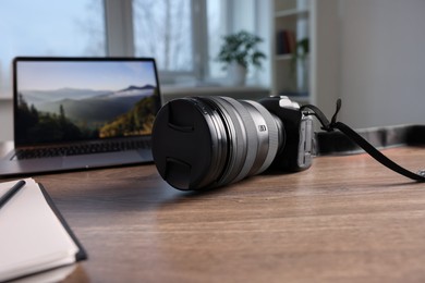 Photo of Professional photo camera, laptop and notepad on wooden desk indoors