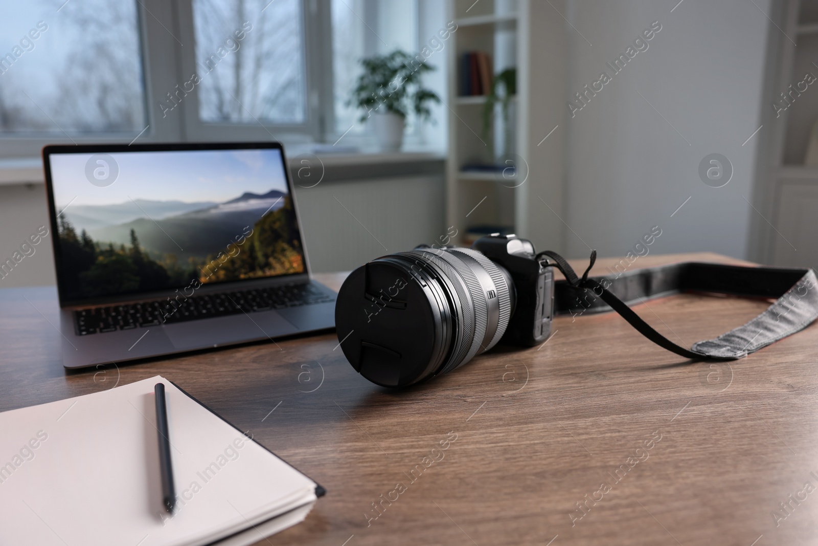 Photo of Professional photo camera, laptop and notepad on wooden desk indoors