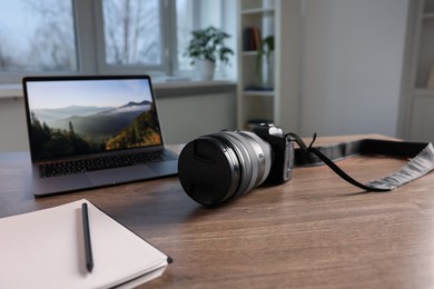 Photo of Professional photo camera, laptop and notepad on wooden desk indoors