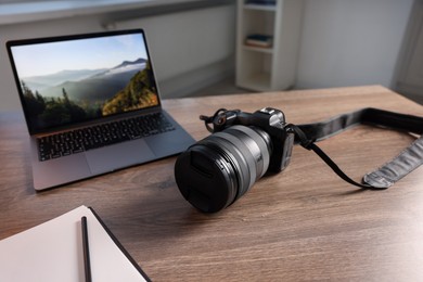 Photo of Professional photo camera, laptop and notepad on wooden desk indoors