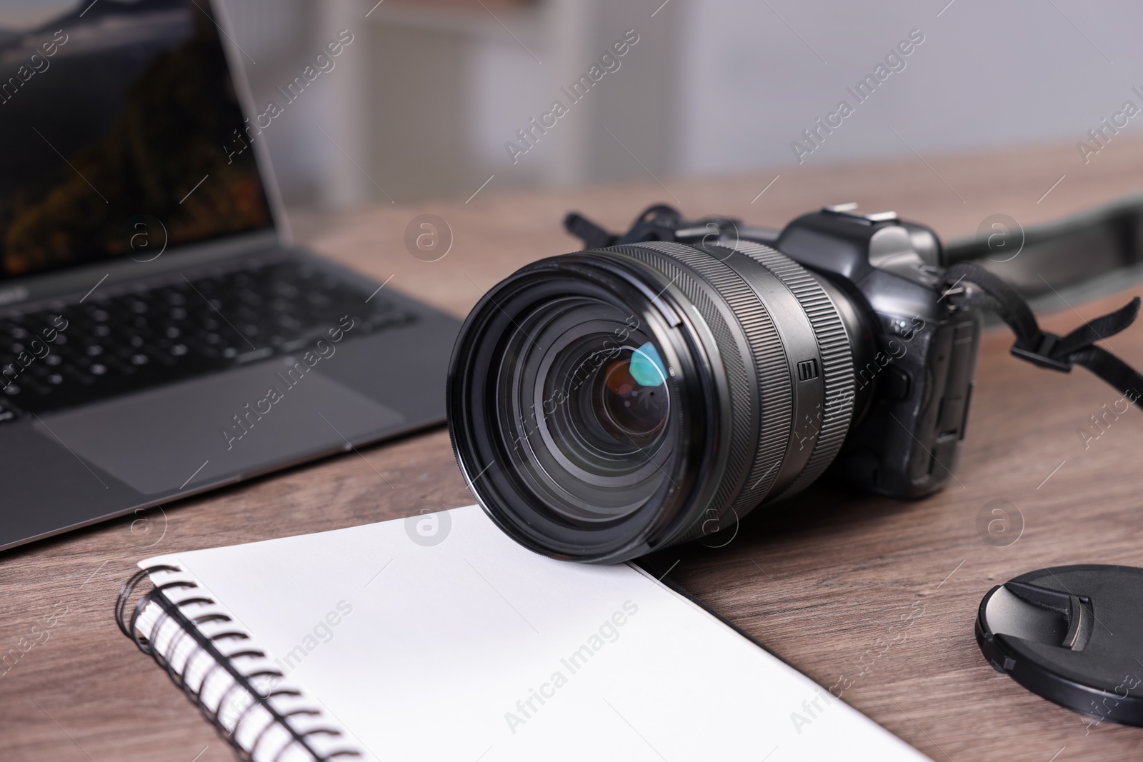 Photo of Professional photo camera, laptop and notepad on wooden desk indoors, closeup