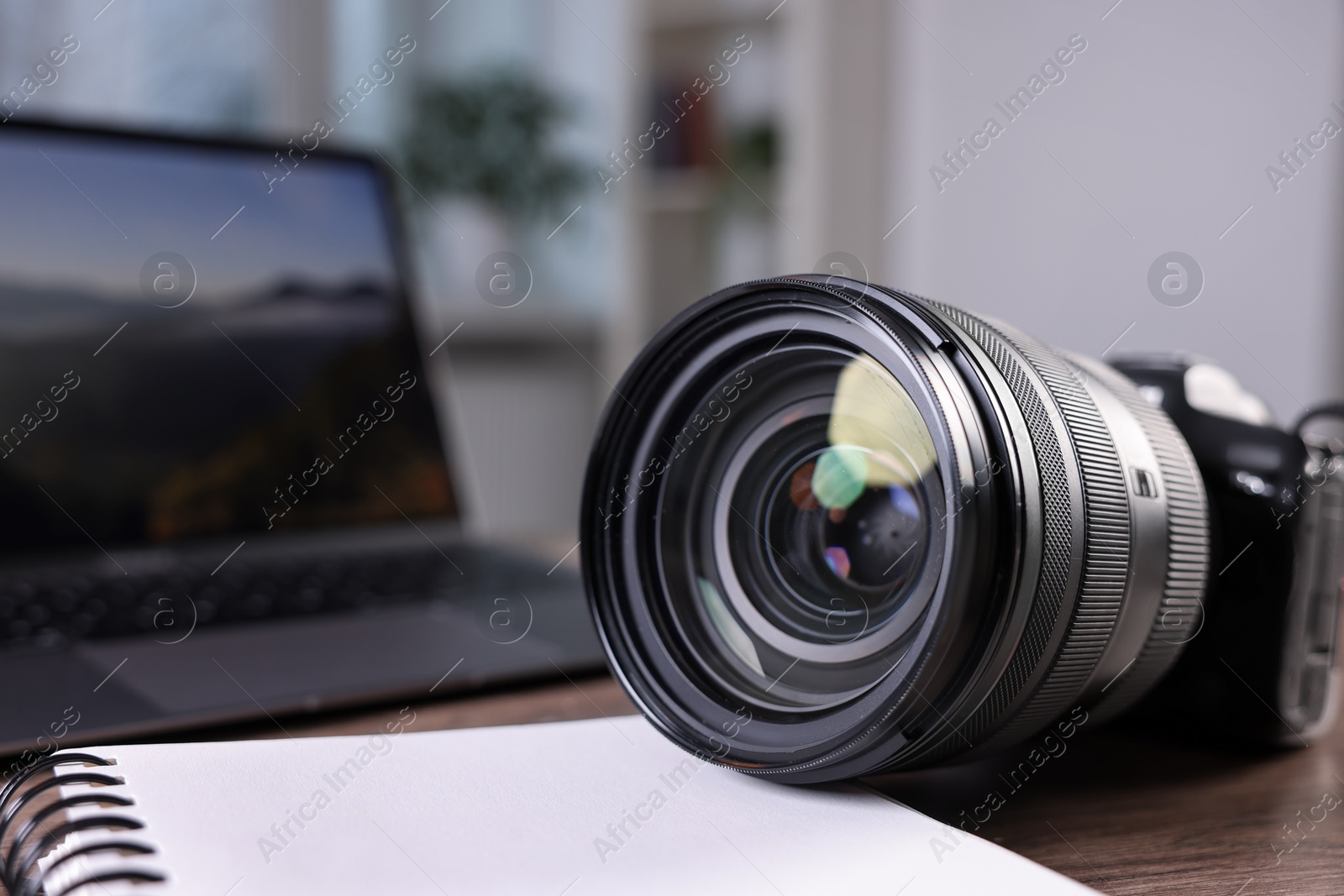 Photo of Professional photo camera, laptop and notepad on wooden desk, closeup