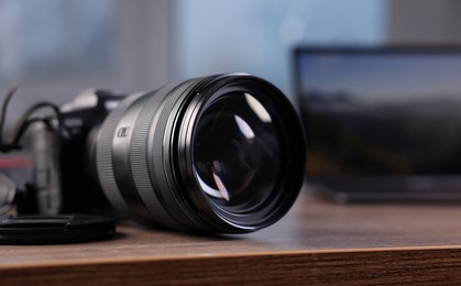 Photo of Professional photo camera and laptop on wooden desk indoors, selective focus