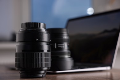 Photo of Professional photo camera lenses and laptop on wooden desk, closeup