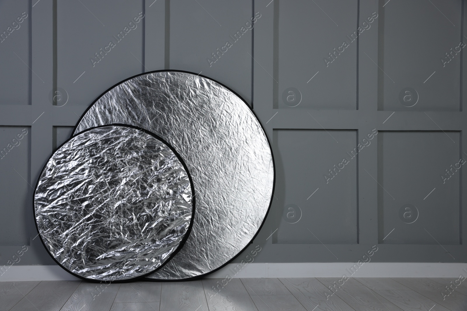 Photo of Professional reflectors on floor near grey wall, space for text. Photo studio equipment