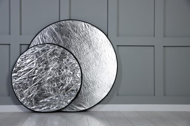 Photo of Professional reflectors on floor near grey wall, space for text. Photo studio equipment