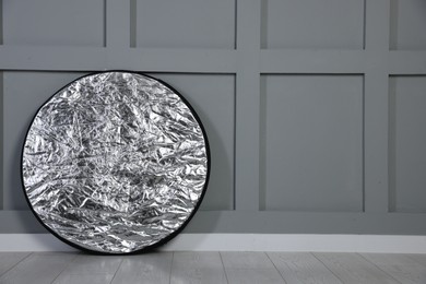 Photo of Professional reflector on floor near grey wall, space for text. Photo studio equipment