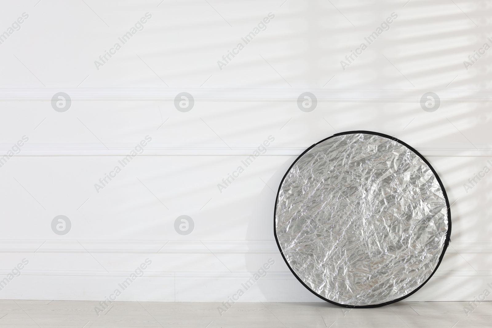 Photo of Professional reflector on floor near white wall, space for text. Photo studio equipment