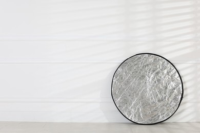 Photo of Professional reflector on floor near white wall, space for text. Photo studio equipment