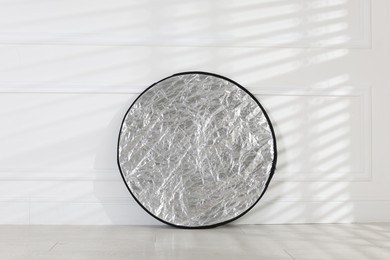 Photo of Professional reflector on floor near white wall. Photo studio equipment