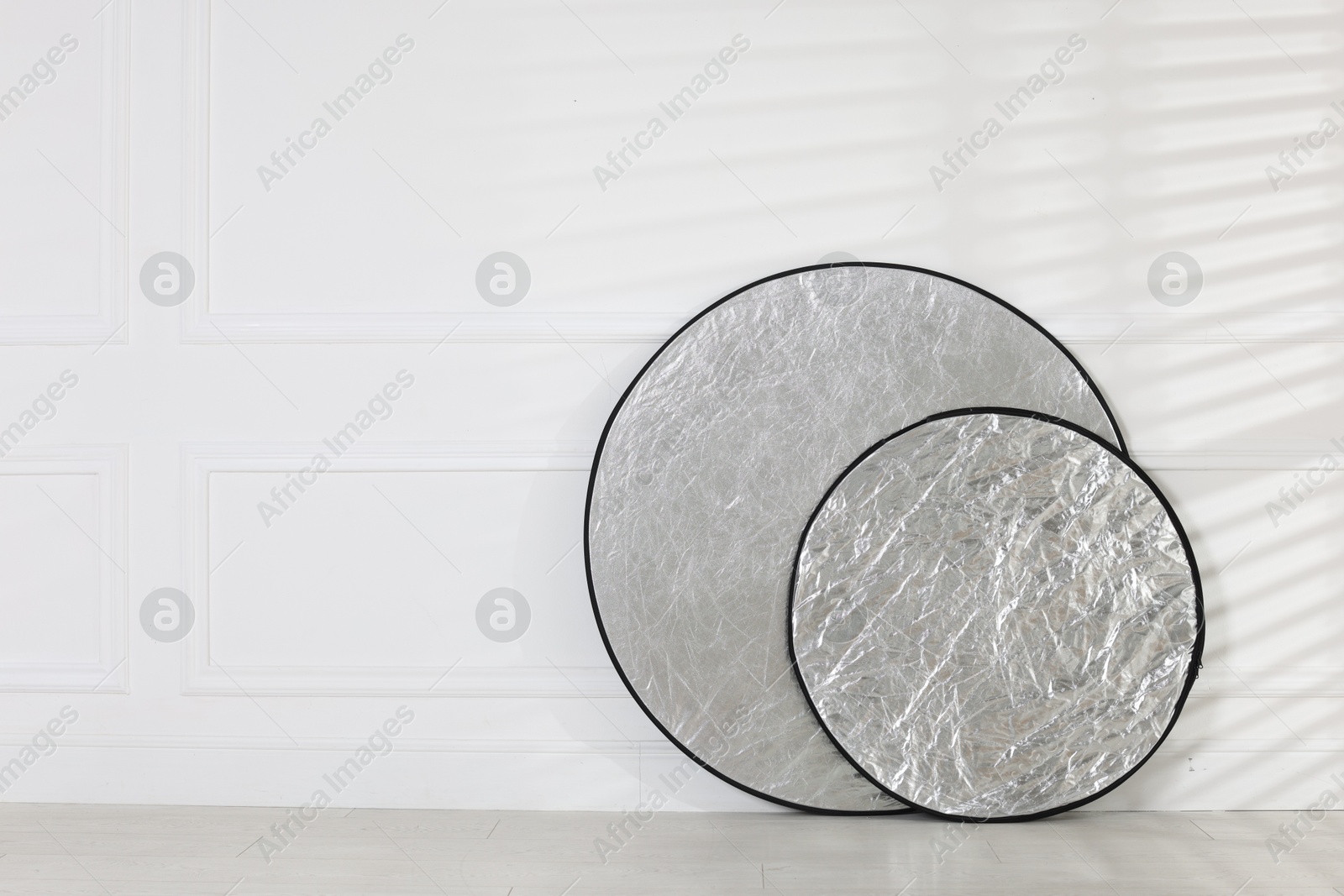 Photo of Professional reflectors on floor near white wall, space for text. Photo studio equipment