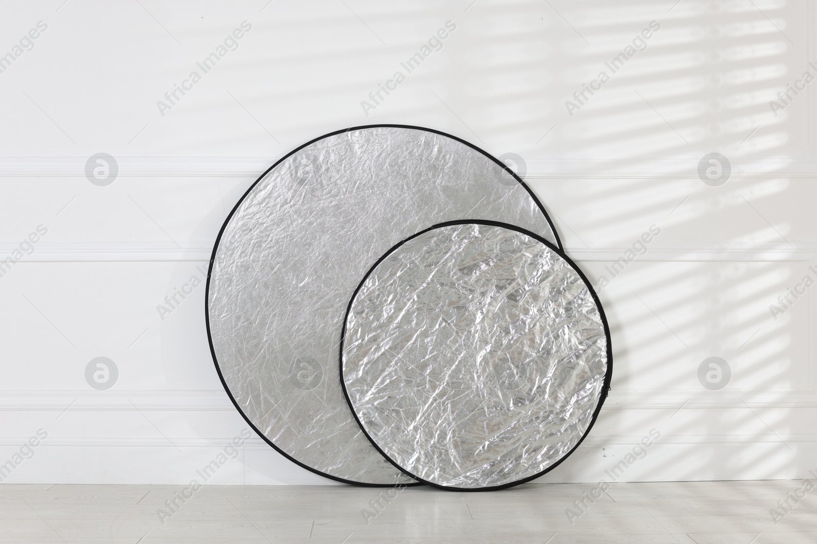 Photo of Professional reflectors on floor near white wall. Photo studio equipment