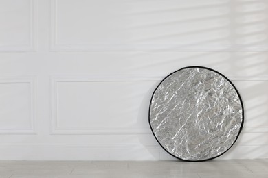 Photo of Professional reflector on floor near white wall, space for text. Photo studio equipment