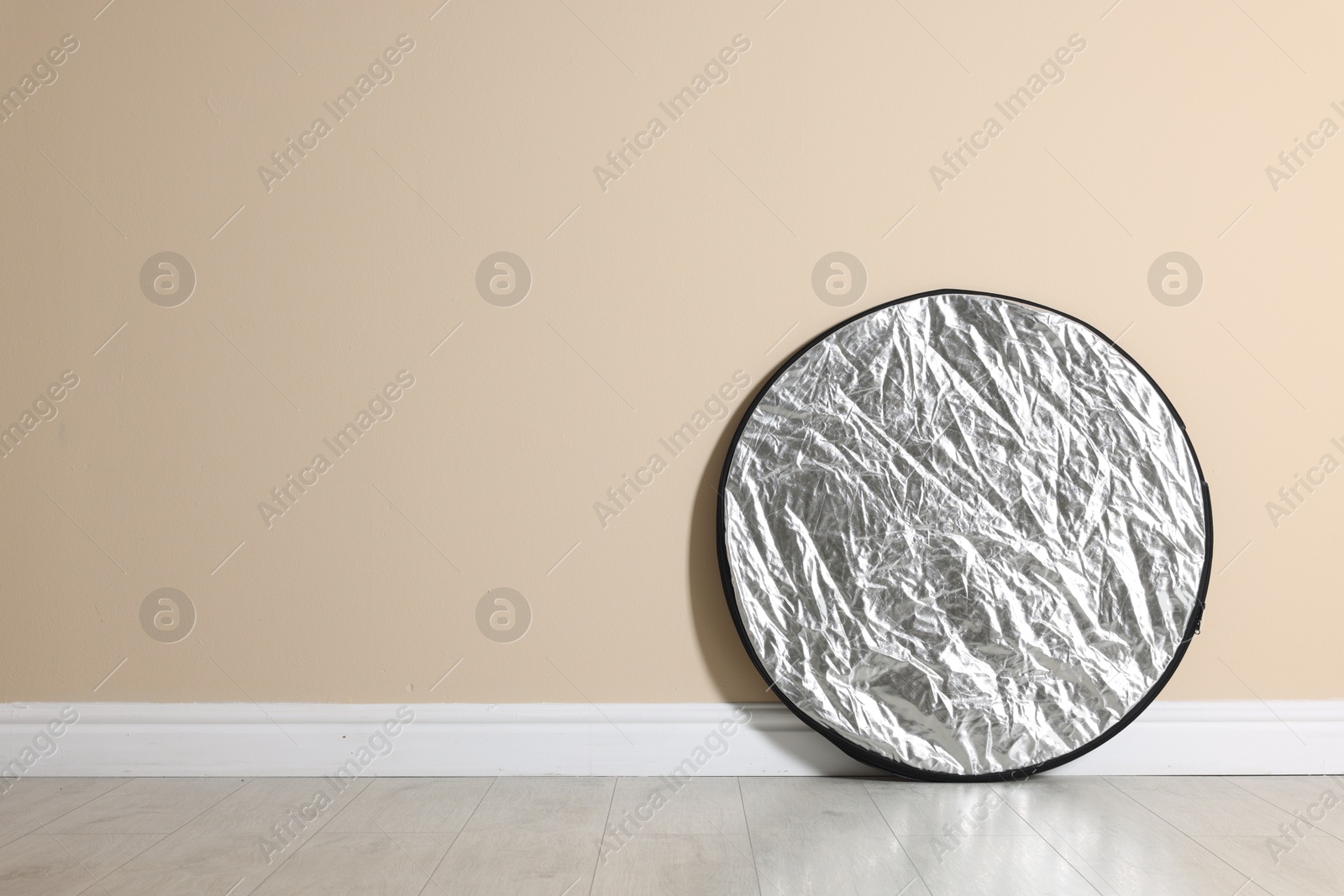 Photo of Professional reflector on floor near beige wall, space for text. Photo studio equipment