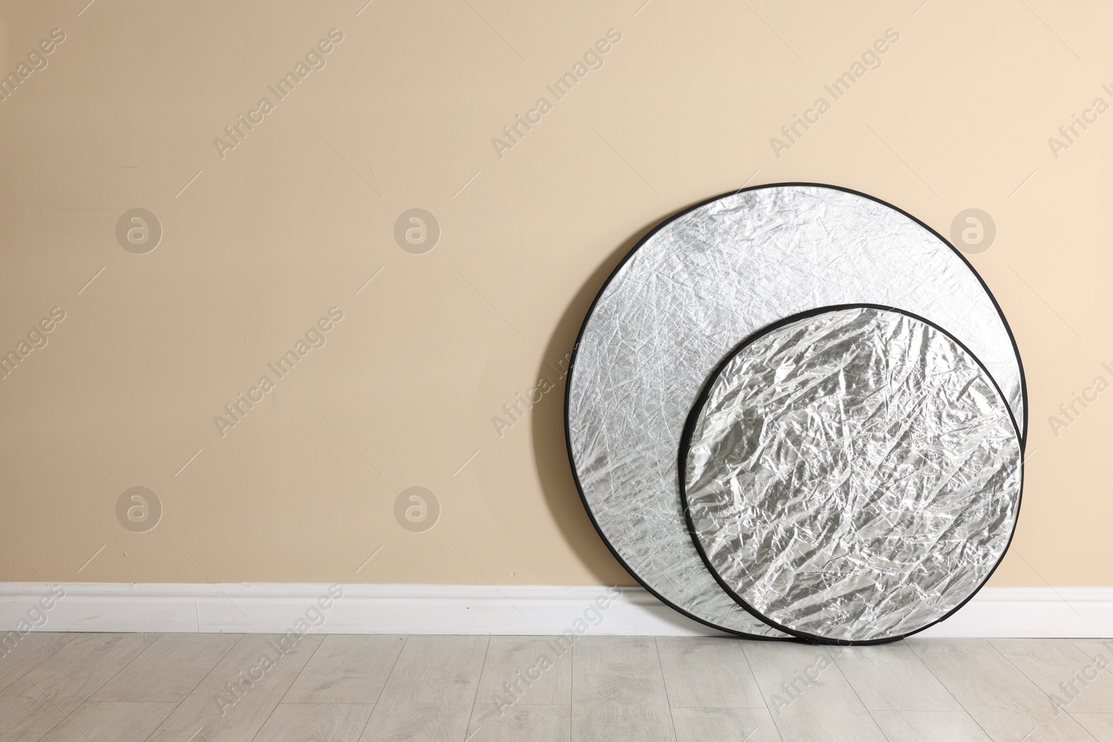 Photo of Professional reflectors on floor near beige wall, space for text. Photo studio equipment