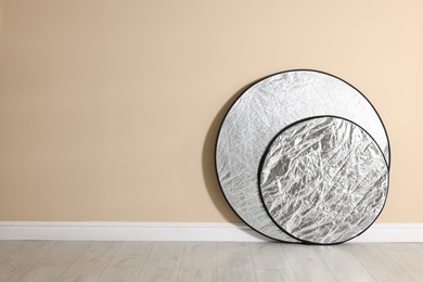 Photo of Professional reflectors on floor near beige wall, space for text. Photo studio equipment