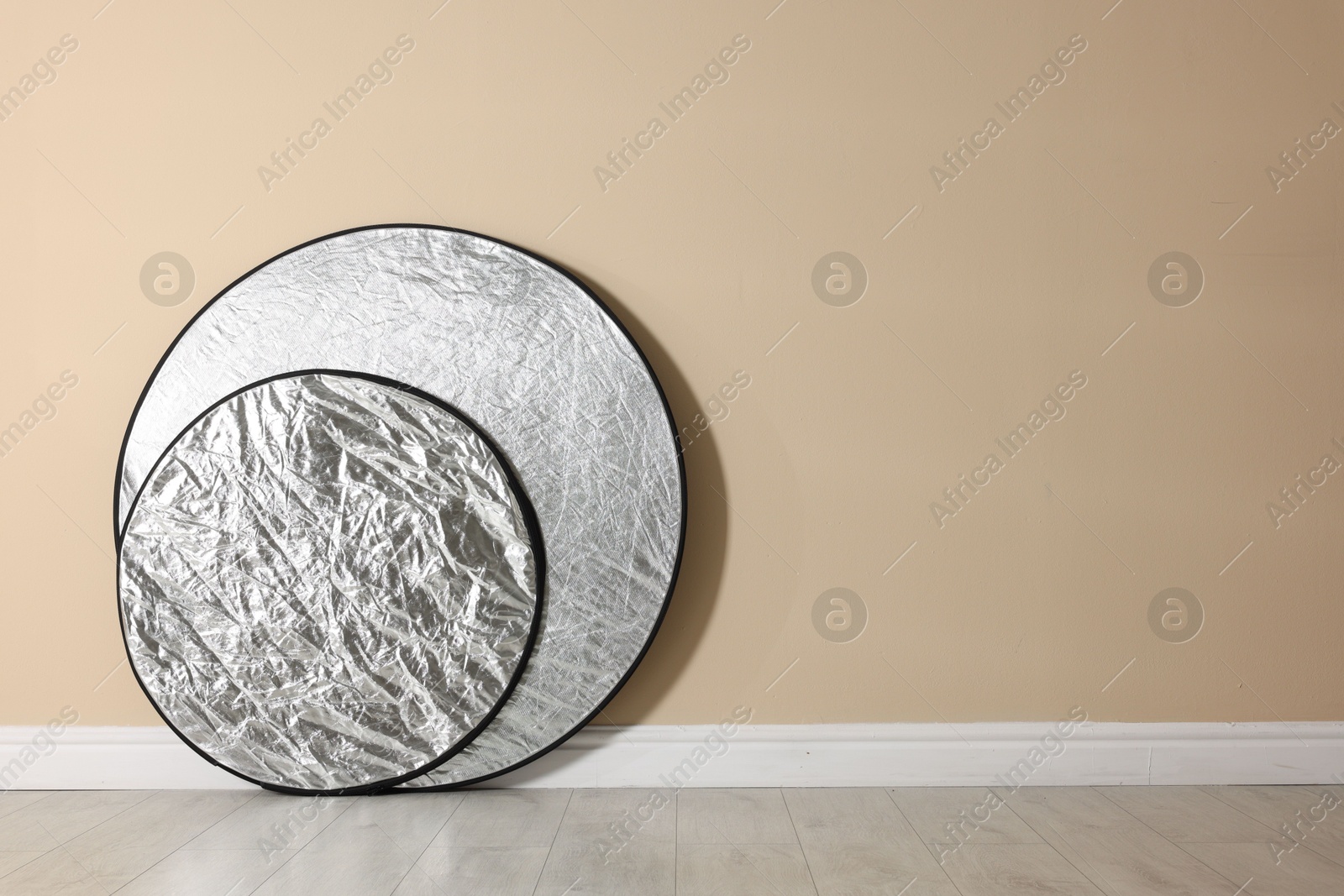 Photo of Professional reflectors on floor near beige wall, space for text. Photo studio equipment