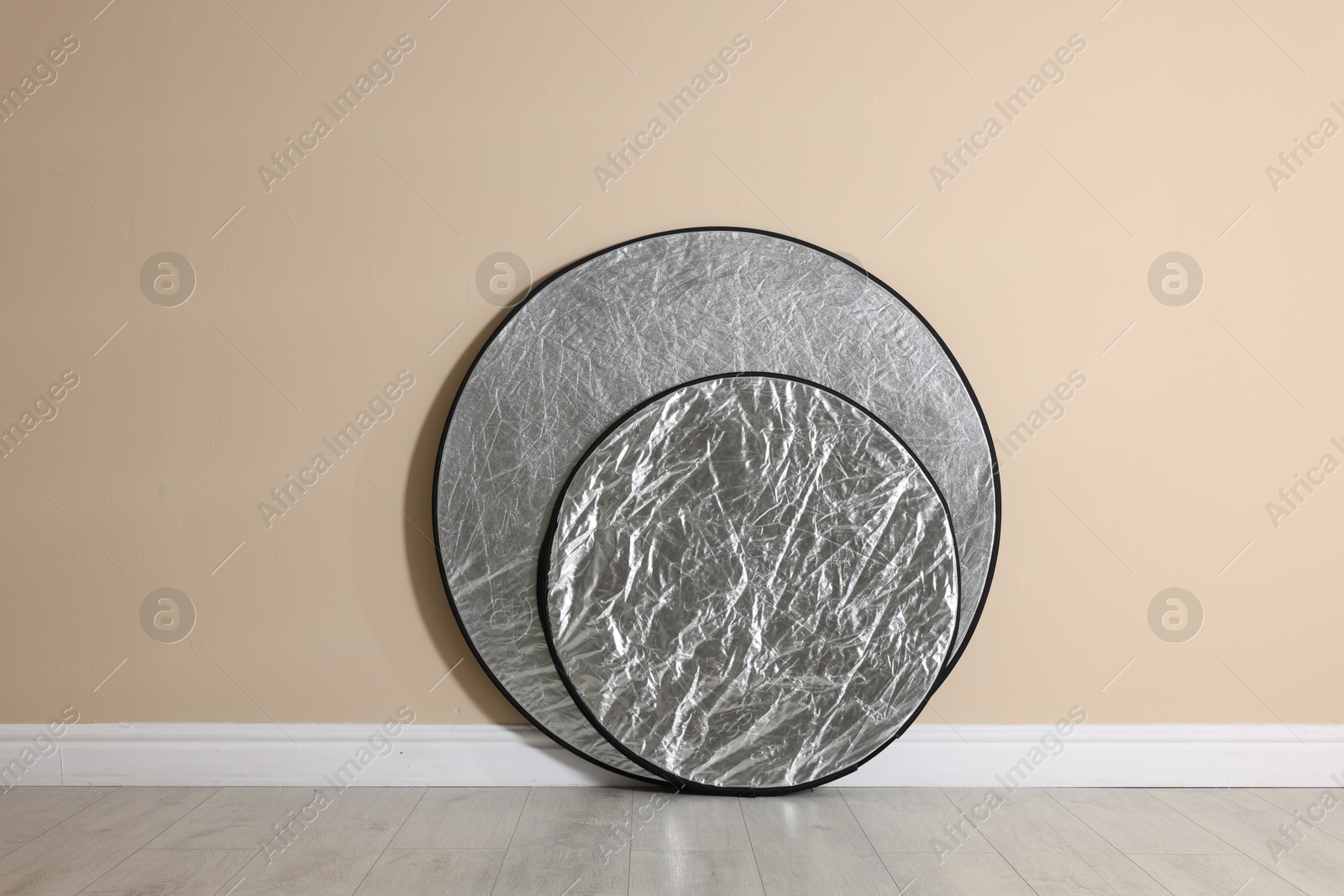 Photo of Professional reflectors on floor near beige wall. Photo studio equipment