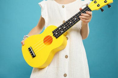 Photo of Little girl with ukulele on light blue background, closeup