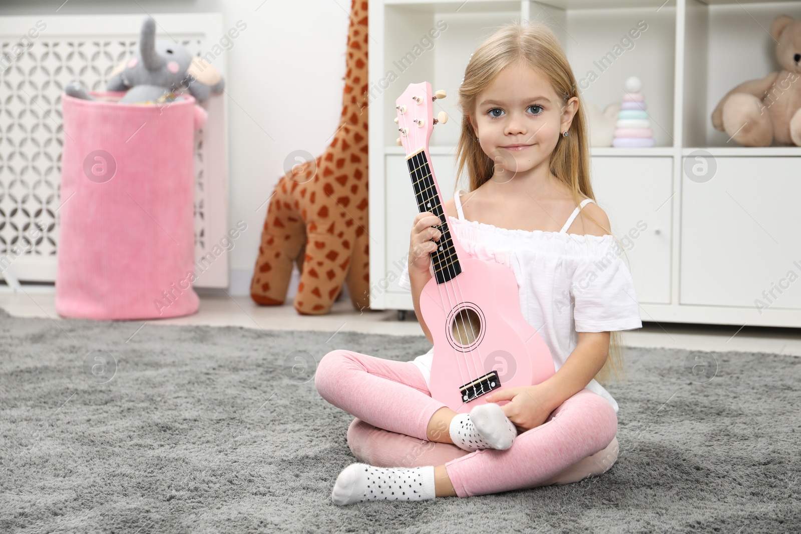 Photo of Little girl with pink ukulele at home