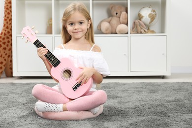 Photo of Little girl with pink ukulele at home