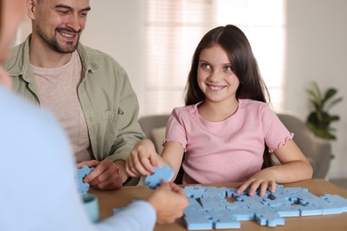 Photo of Happy parents and their daughter solving puzzle together at wooden table indoors