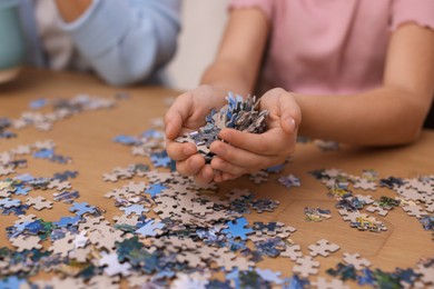 Photo of Mother and her daughter solving puzzle together at wooden table indoors, closeup