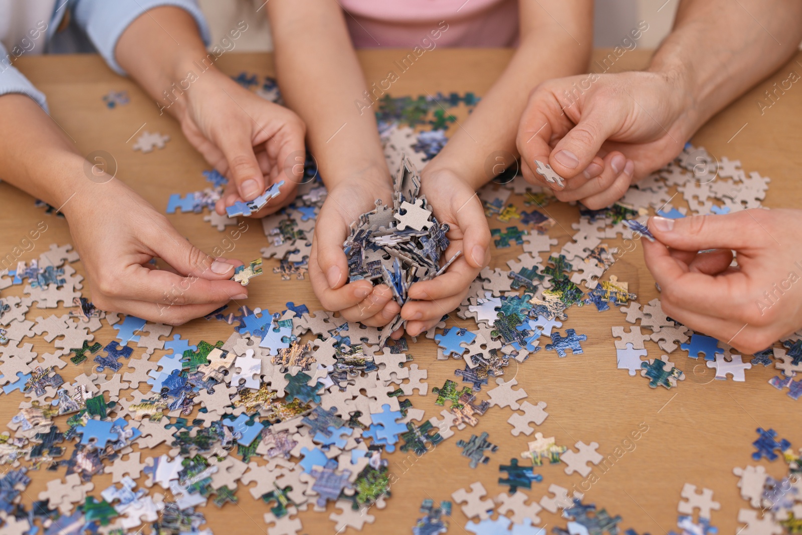 Photo of Parents and their daughter solving puzzle together at wooden table, closeup