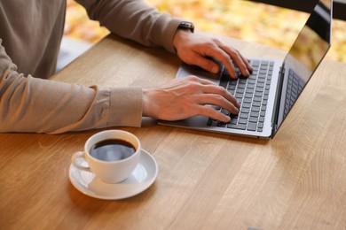 Photo of Man working on laptop at wooden table in cafe, closeup