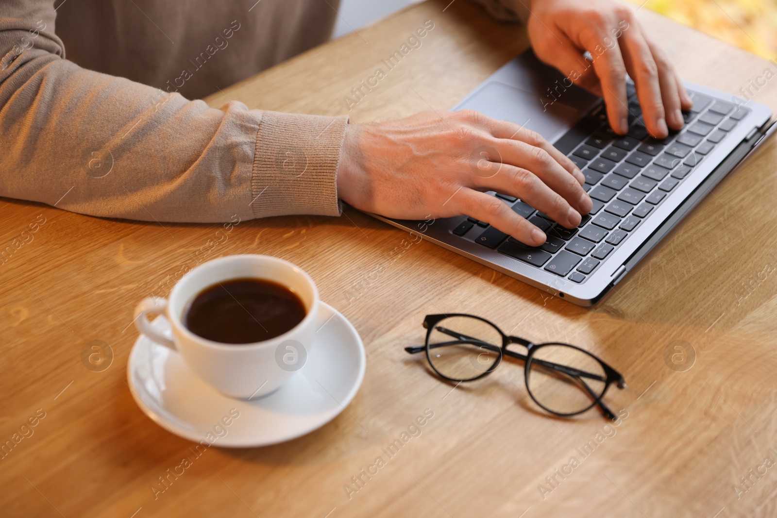 Photo of Man working on laptop at wooden table in cafe, closeup