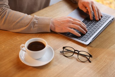 Photo of Man working on laptop at wooden table in cafe, closeup