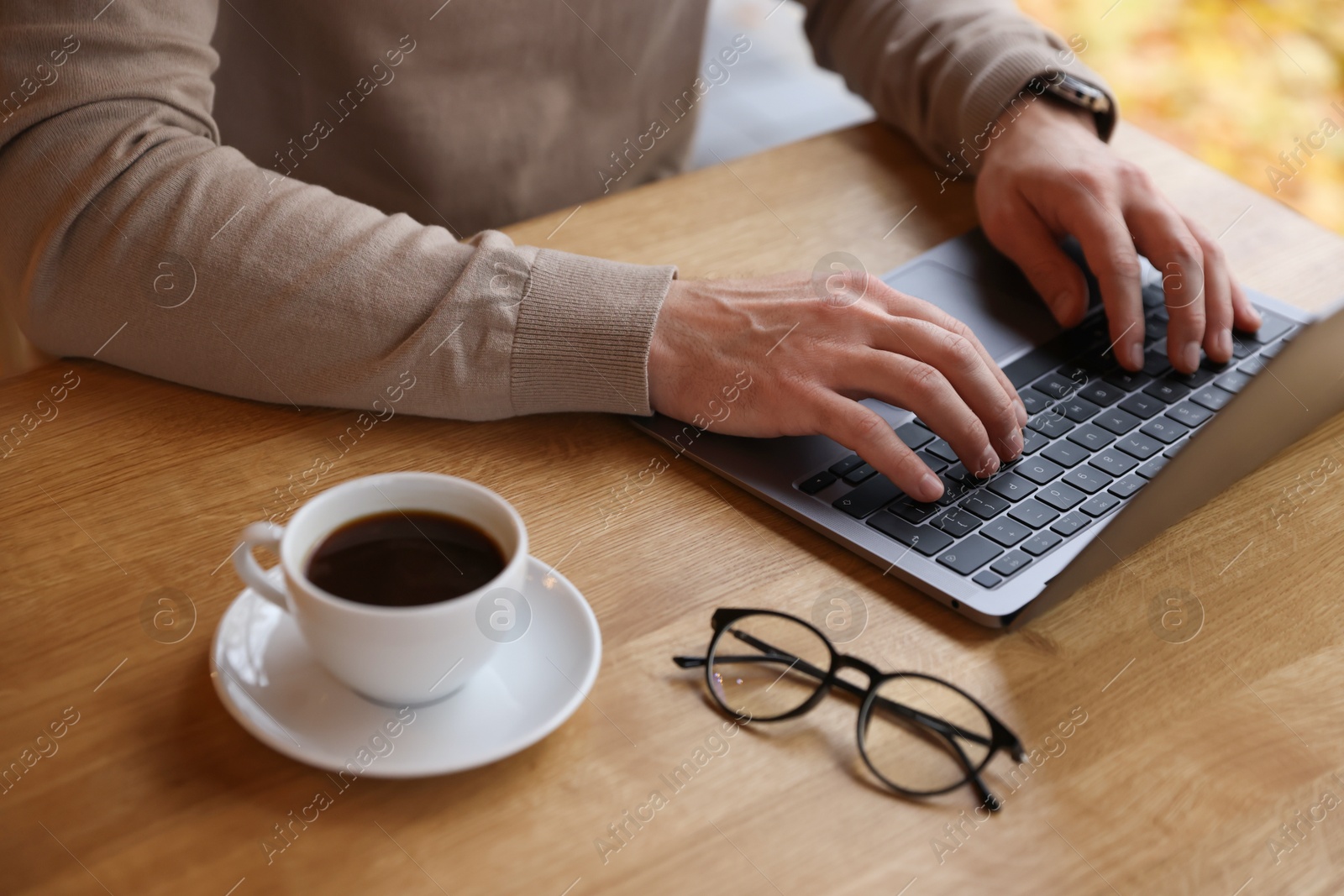 Photo of Man working on laptop at wooden table in cafe, closeup