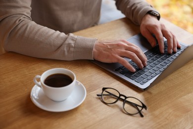 Photo of Man working on laptop at wooden table in cafe, closeup