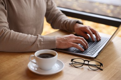 Photo of Man working on laptop at wooden table in cafe, closeup